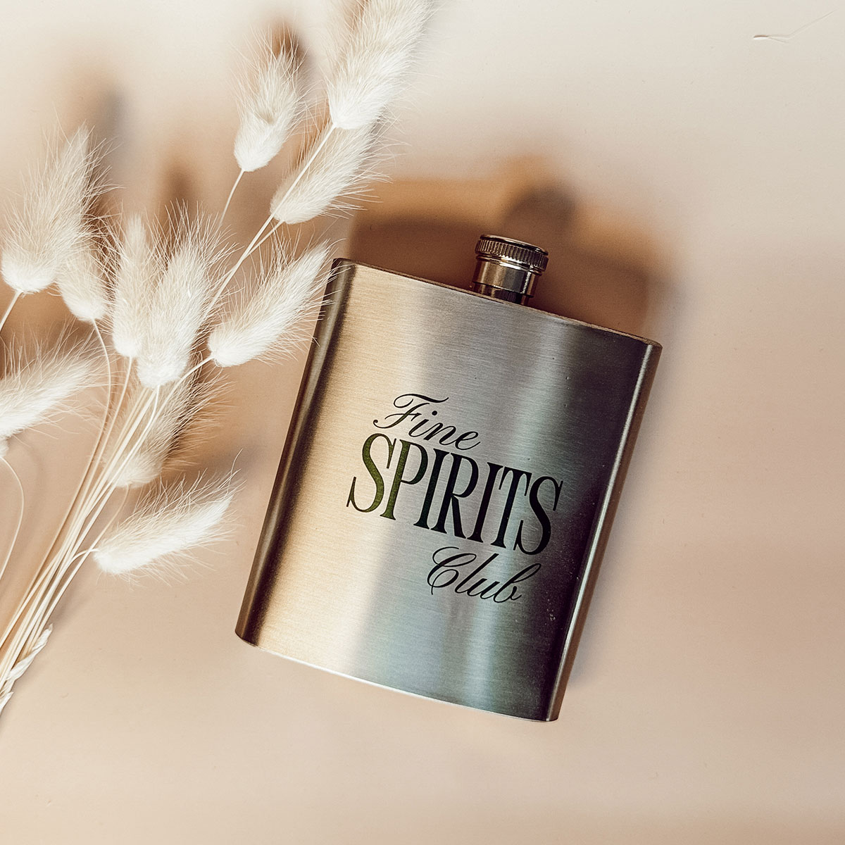 Edelstahl-Flachmann mit Fine Spirits Club Motiv, dekoriert mit hellem Pampasgras