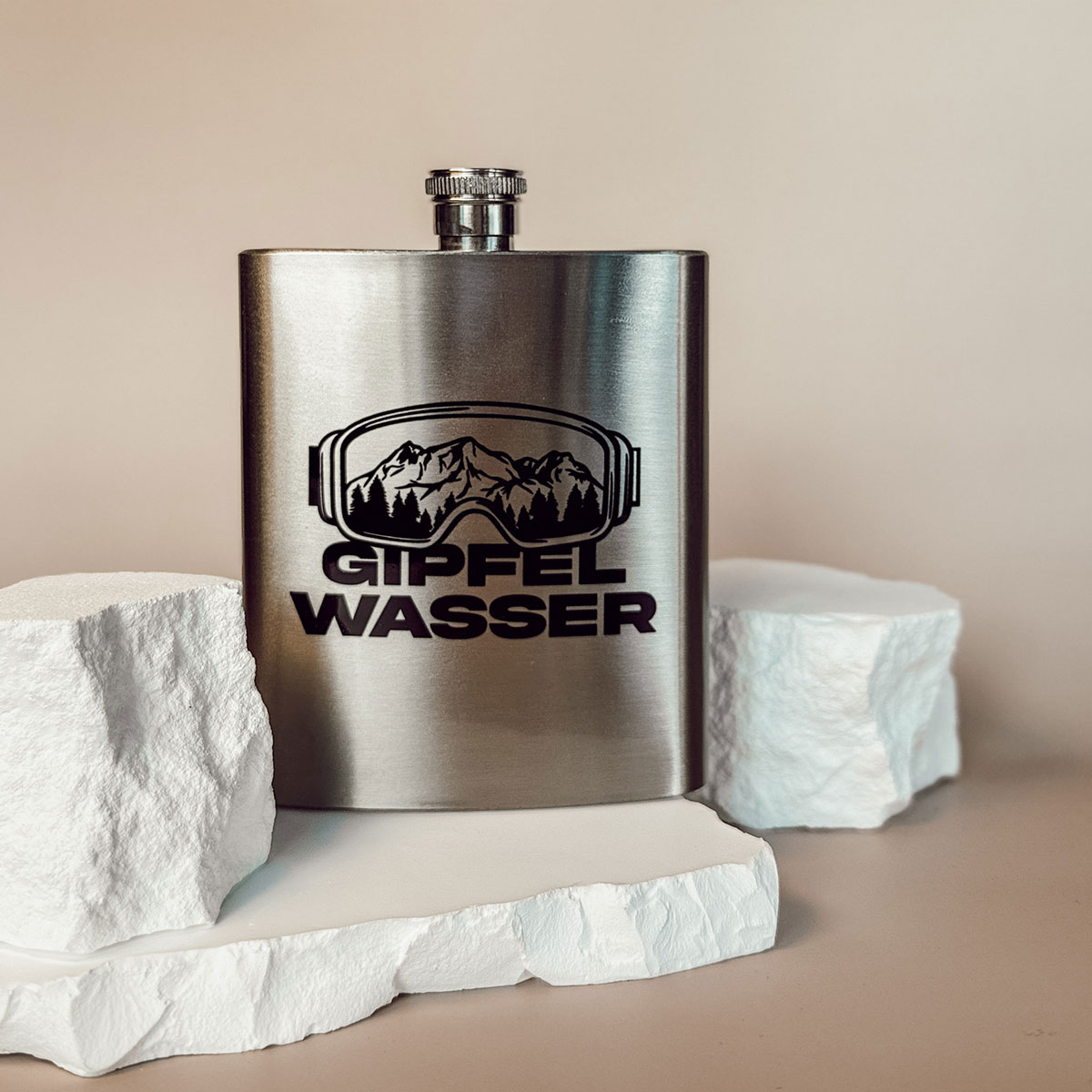 Edelstahl-Flachmann mit Gipfelwasser-Motiv, Berggrafik und Schneebrillen-Design vor hellem Hintergrund