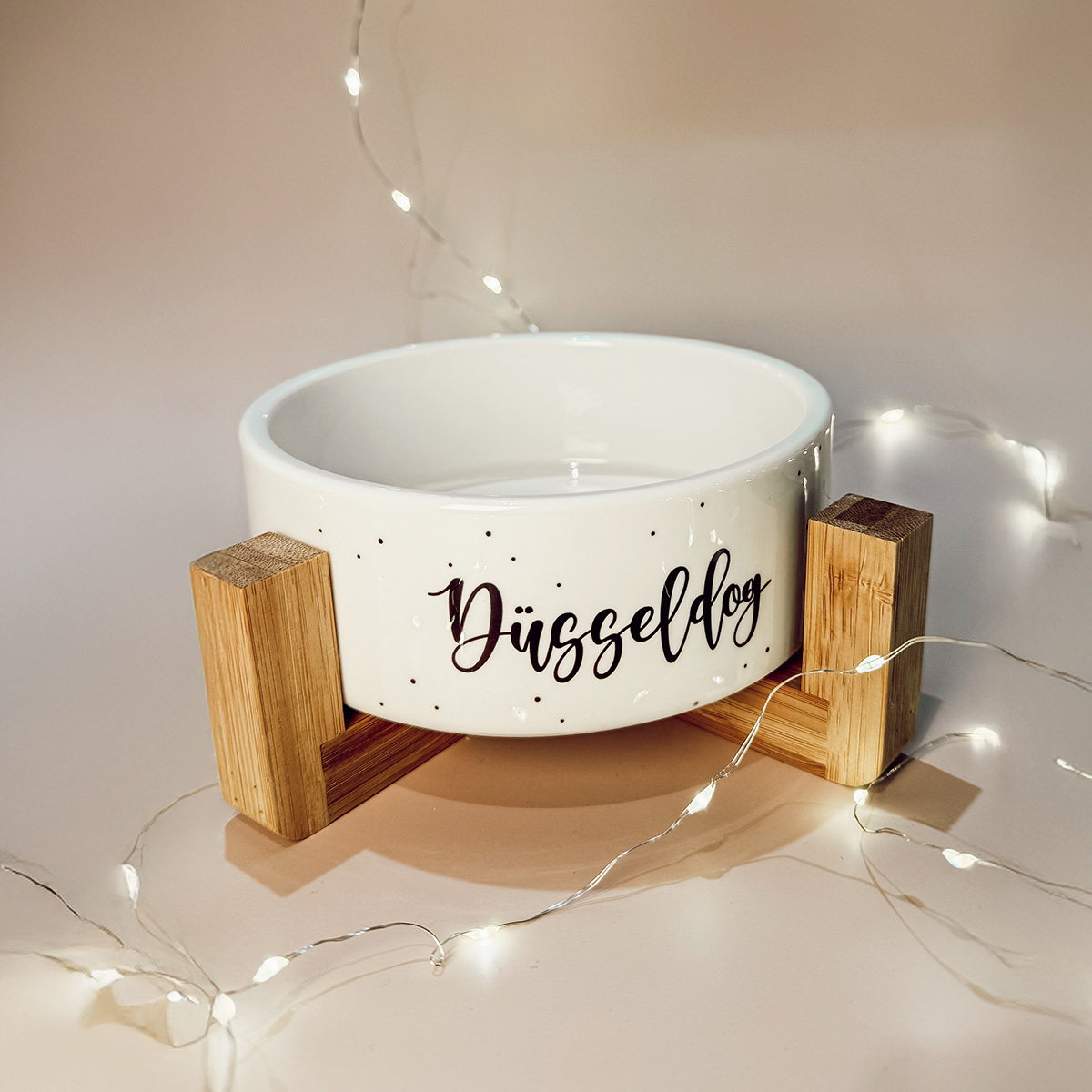 Weißer Keramik-Hundenapf mit Holzständer und Düsseldog Schriftzug, dekoriert mit Lichterkette