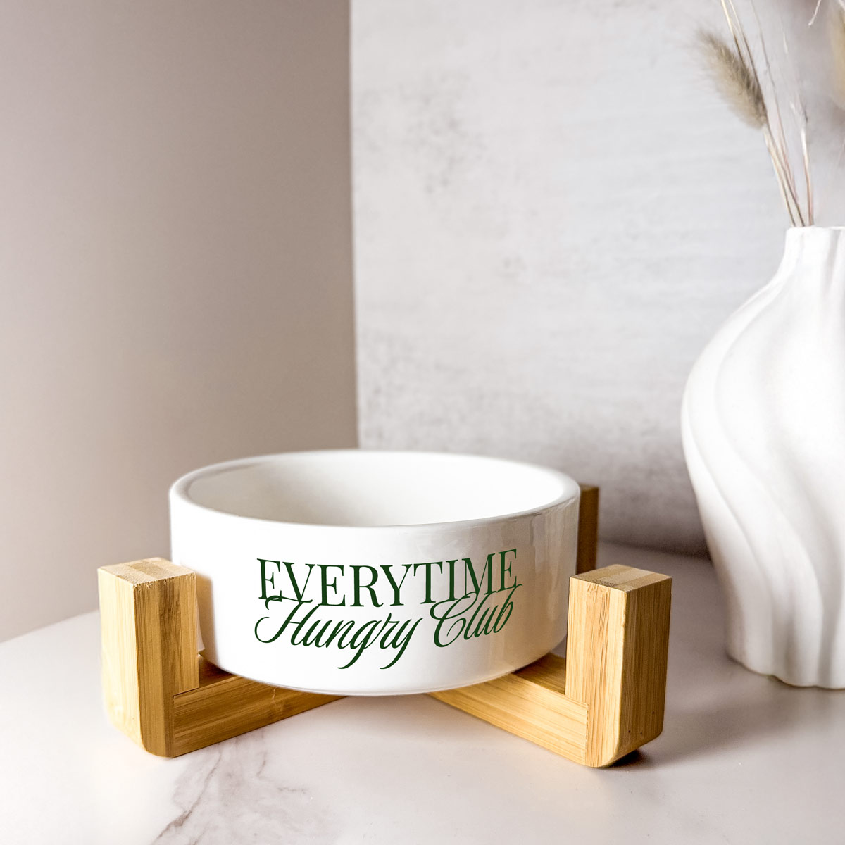 Keramik-Napf mit grünem Schriftzug „Everytime Hungry Club“ in einem modernen Holzständer.