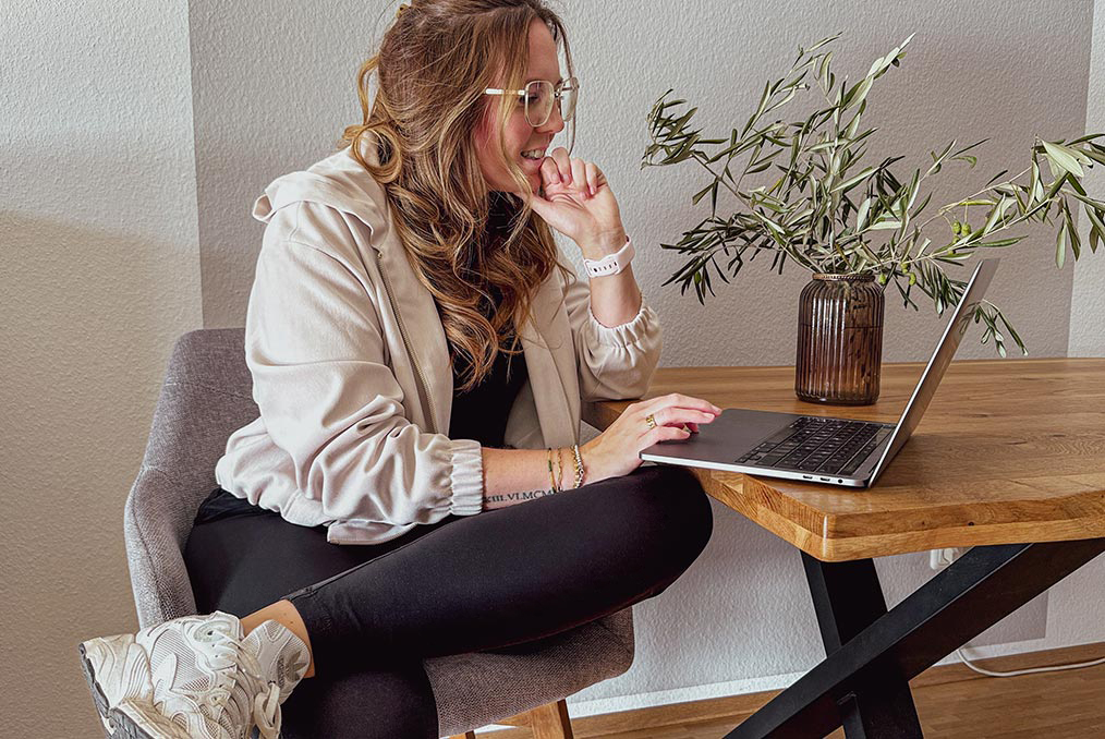 Andra Kaiser arbeitet entspannt am Laptop an einem Holztisch mit einer Vase und Olivenzweigen