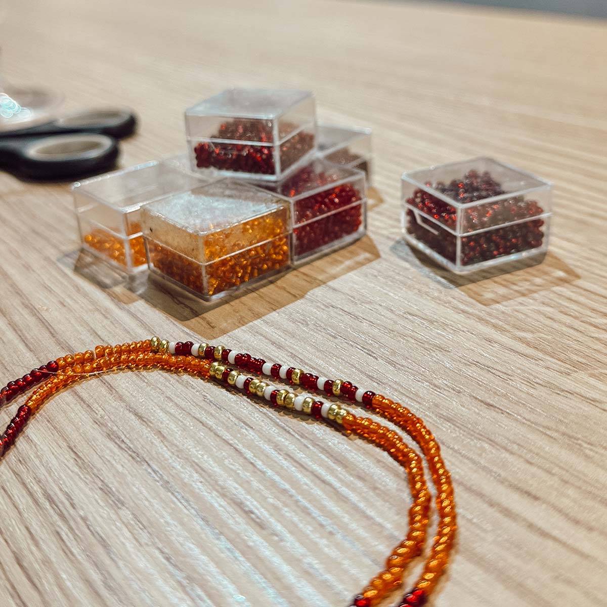 Auswahl an bunten Glasperlen in Rot- und Orangetönen und ein gefädeltes Armband beim Perlen-Workshop in Düsseldorf