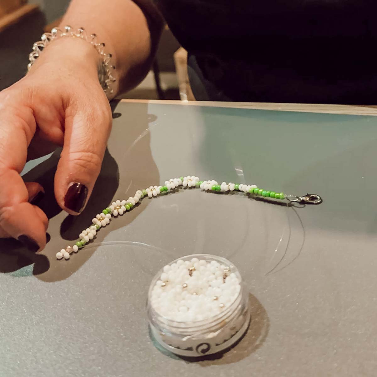 Teilnehmerin beim Perlen-Workshop in Düsseldorf fädelt ein Armband aus weißen und grünen Perlen
