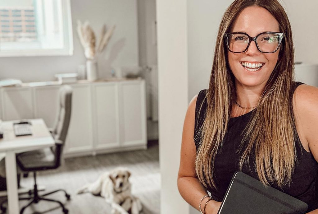 Andra Kaiser arbeitet entspannt am Laptop an einem Holztisch mit einer Vase und Olivenzweigen