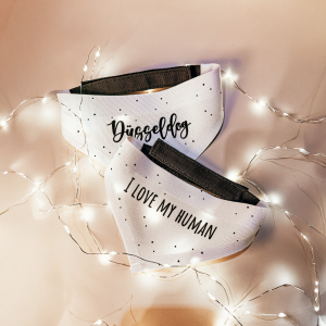 Zwei weiße Hundebandanas mit den Aufdrucken „Düsseldog“ und „I Love My Human“, dekoriert mit Lichterkette