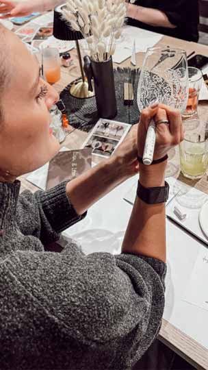 Teilnehmerin bemalt ein Weinglas im Kreativworkshop.