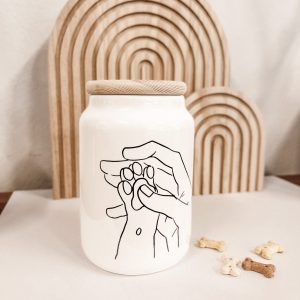 Weiße Keramik Leckerlidose mit Bambusdeckel und gezeichnetem Pfoten-Motiv, gefüllt mit Hundeleckerlis, Produkt von zehn null zwo.