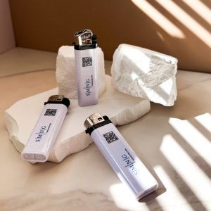 Drei weiße nachfüllbare Feuerzeuge mit UV Druck und Logo, dekorativ fotografiert auf Stein im Licht, Produkt von zehn null zwo.