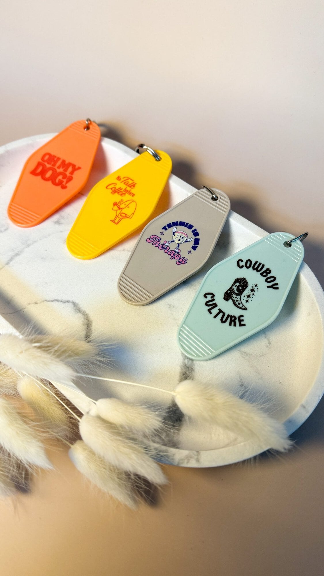 Vier bunte Motel Keychains mit unterschiedlichen UV-Druck Designs liegen dekorativ auf einer Marmorplatte