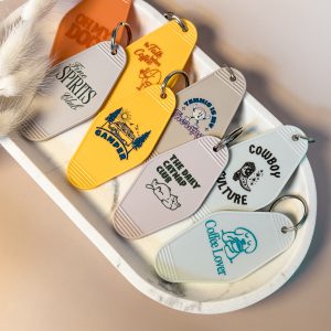 Vier bunte Motel Keychains mit unterschiedlichen UV-Druck Designs liegen dekorativ auf einer Marmorplatte