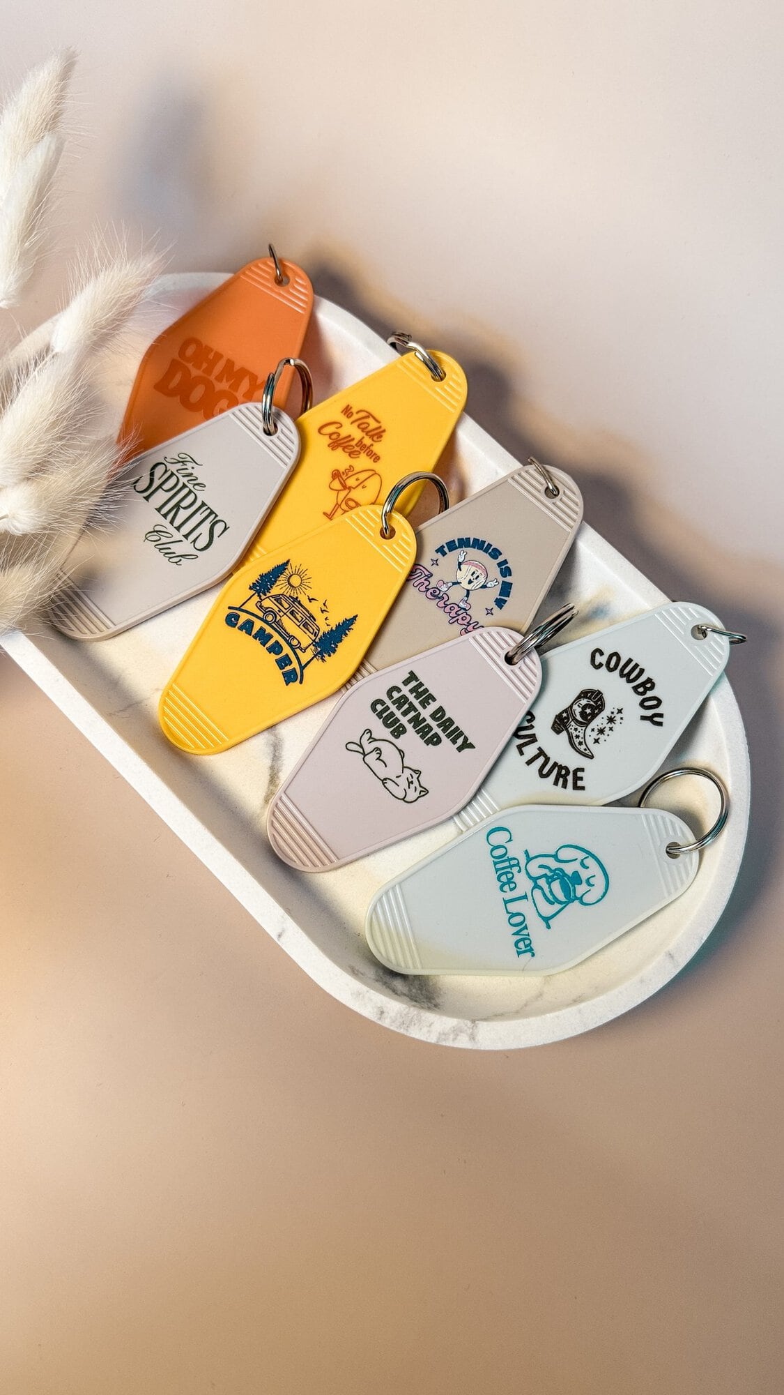 Vier bunte Motel Keychains mit unterschiedlichen UV-Druck Designs liegen dekorativ auf einer Marmorplatte